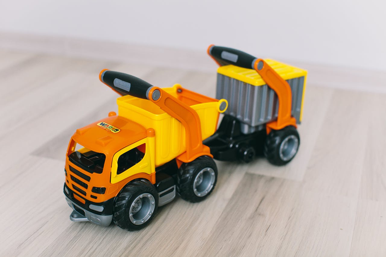 creative-03 Bright orange and yellow toy dump truck on light wooden floor, close-up view.