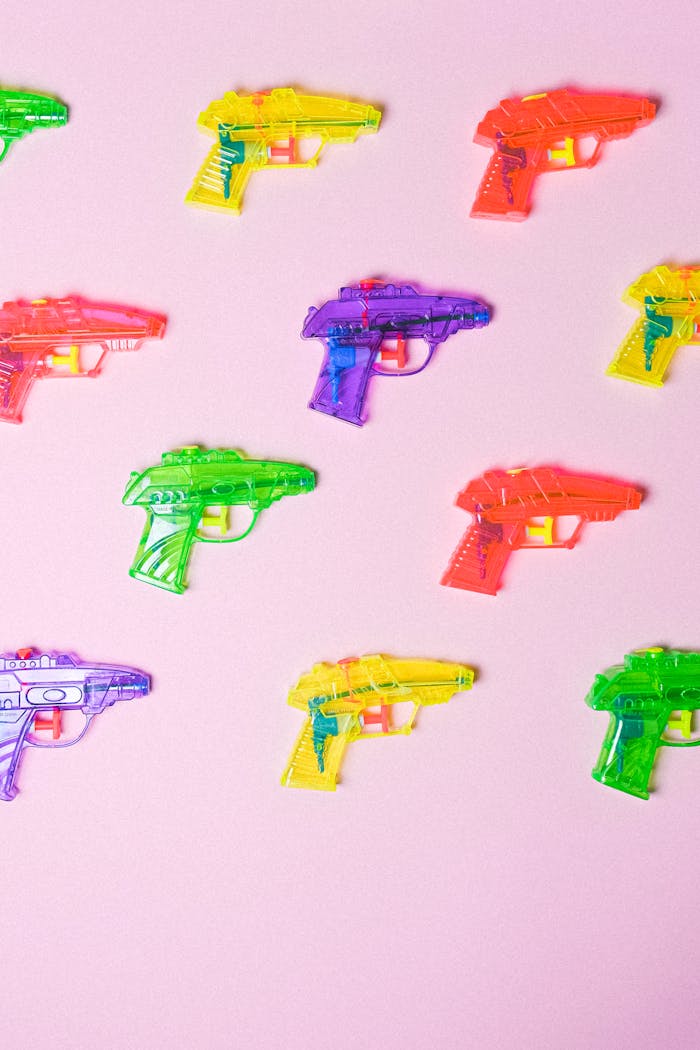brand-03 Colorful toy water guns on a pink background arranged in a pattern.