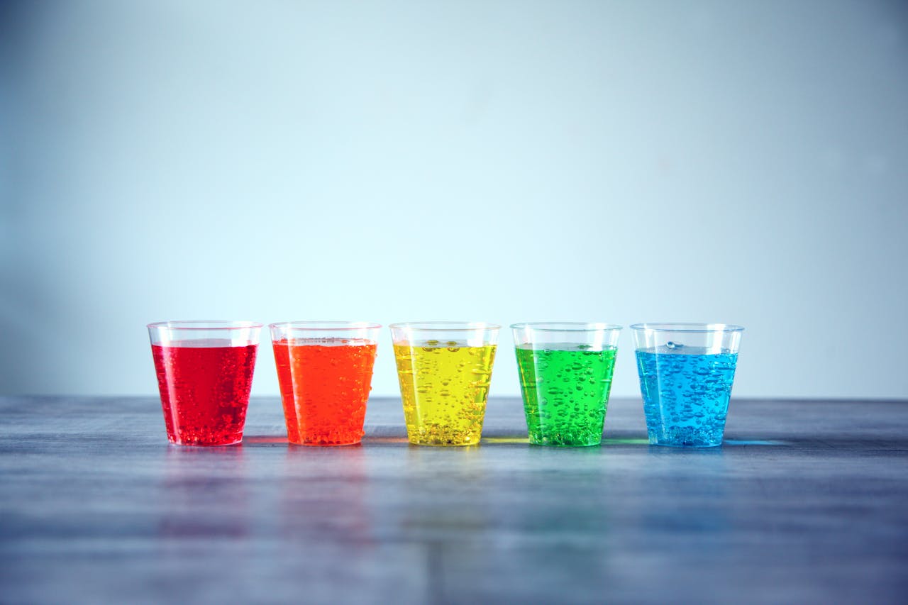 brand-02 Five colorful fizzy drinks in plastic cups organized in a row indoors.